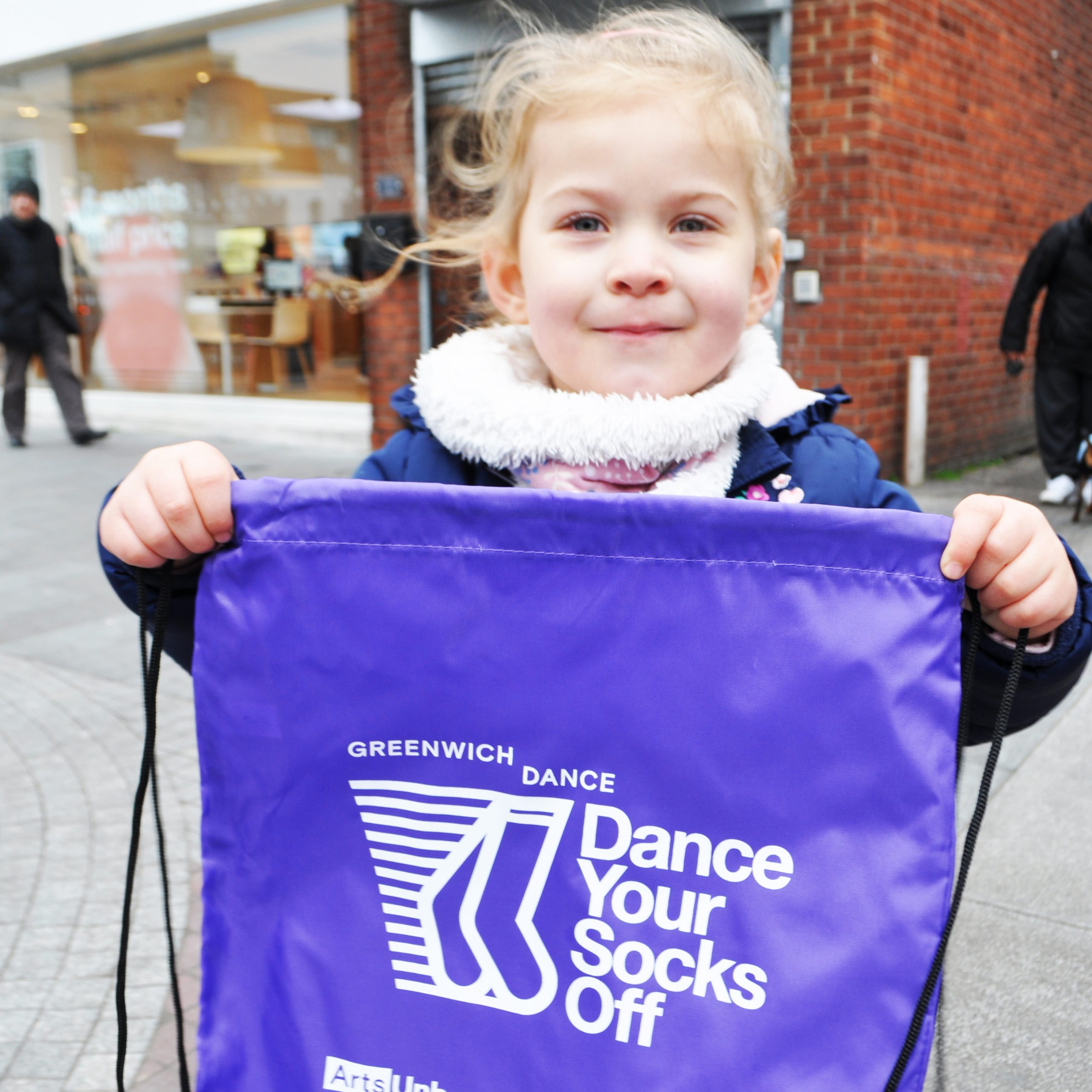 Dance Your Socks Off. A young girl holds up a purple bag with the Dance Your Socks Off logo printed on it